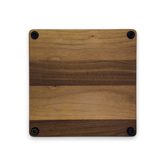 The Maple 12 x 12" Walnut Square Board features light and dark horizontal stripes and four black rubber feet on each corner, shown against a white background.