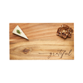 The Maple 14 x 8" Acacia Modern Rectangle Board with “grateful” script displays a wedge of herb-garnished cheese on the left and multigrain crackers on the right.
