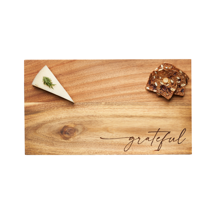 The Maple 14 x 8" Acacia Modern Rectangle Board with “grateful” script displays a wedge of herb-garnished cheese on the left and multigrain crackers on the right.