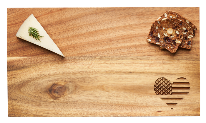The Maple 14 x 8" Acacia Modern Rectangle Board | Patriotic Heart features a wedge of herb-topped cheese on the left, seeded crackers on the right, and a patriotic heart carving in the bottom right corner.