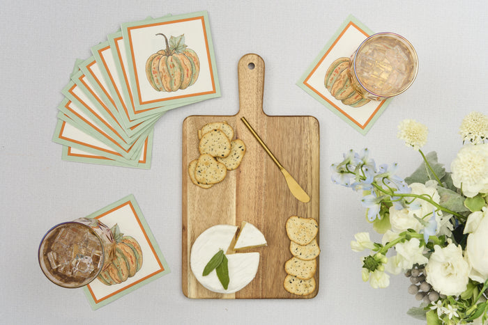 The Sophistiplate 14" x 8" Board Gift Kit: Bright & Thankful holds round cheese, crackers, and a gold knife. Pumpkin floral napkins, two iced drinks, and white flowers with greenery finish this charming tablescape.