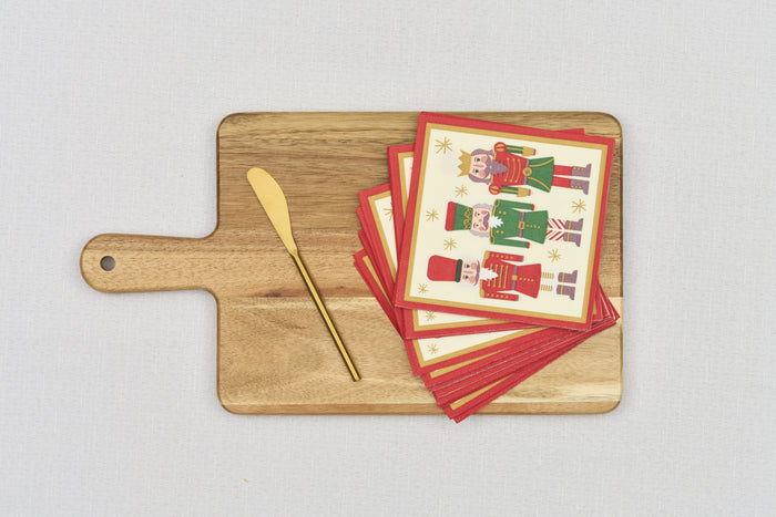 The Sophistiplate 14" x 8" Board Gift Kit: Nutcracker Christmas features a wooden cheese board, gold knife, and festive red-bordered Nutcracker napkins, all displayed on a light grey surface.