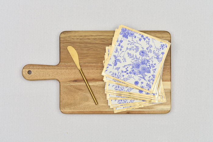 The Sophistiplate 14" x 8" Board Gift Kit: Timeless, featuring a wooden cheese board, gold butter knife, and blue and white floral napkins, rests on a light grey surface.