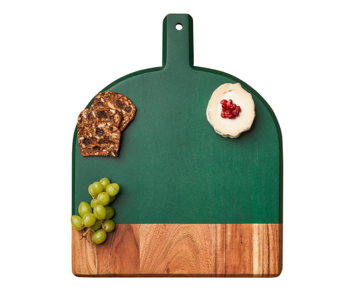 A 15" x 12" Green Acacia Bevel Board w/ Spreader by Maple elegantly displays cheese with red berries, crackers, and green grapes, all neatly arranged in separate corners on this stylish wooden charcuterie board.