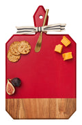 A white background showcases Maple’s 16" x 10" Acacia Heirloom Board in Red with a gold spreader, topped with crackers, cheese cubes, and a halved fig.