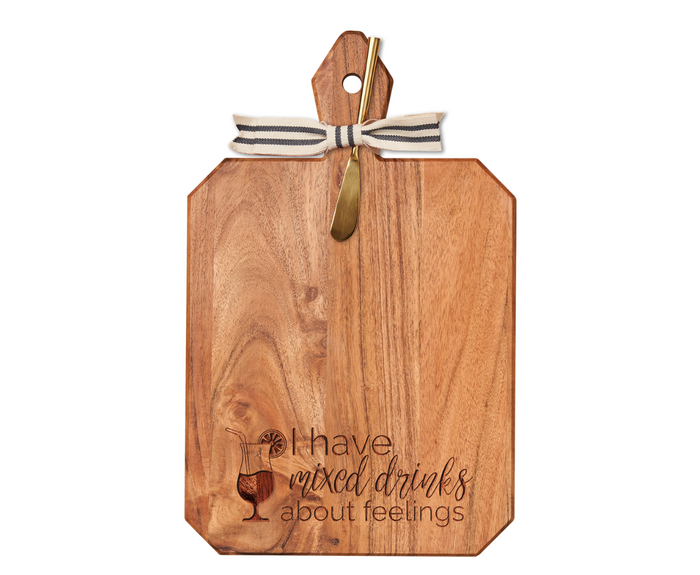 The Maple 16 x 10" Acacia Heirloom Board with Gold Spreader features a striped ribbon, engraved cocktail glass, and "I Have Mixed Drinks About Feelings"—perfect for charcuterie or cocktails.