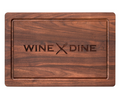 The Maple 18 x 12" Maple Wood Cutting Board | Wine & Dine features an engraved border and a crossed fork and knife with "WINE DINE" at the center—ideal as a stylish charcuterie or cheese board.
