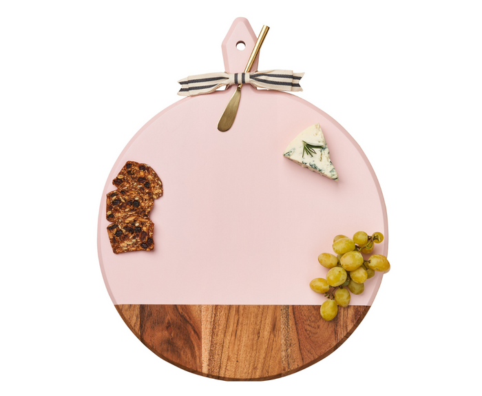 The Maple 20" x 16" Acacia Heirloom Board in Blush features a gold spreader, striped ribbon, crackers, green grapes, and blue cheese slice, beautifully arranged on a white background.