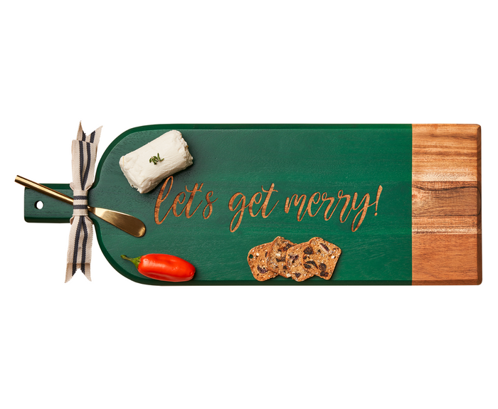 The Maple 20" x 7" Green Acacia Bevel Board w/ Spreader features “Let’s Get Merry!” in gold and is topped with cheese, a gold spreader, red pepper, three crackers, and a striped ribbon around the handle.