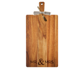 The Maple 24" x 12" Acacia Wood Thick Handle Cutting Board features “Mr & Mrs” engraving, a gold spreader, and a black-and-white striped ribbon, combining elegance and function for your kitchen decor.