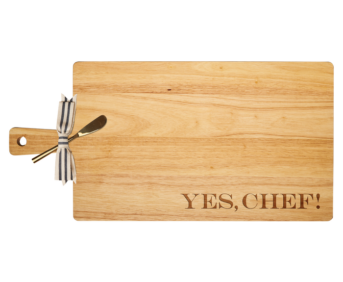 The Maple 24" x 12" Rubber Wood Thick Handle Board features a “YES, CHEF!” engraving and comes with a gold spreader tied with a striped ribbon—ideal as a personalized charcuterie board against a white background.