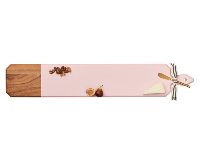 The Maple 34" x 6" Acacia Heirloom Board in Pink features a gold spreader and displays nuts, sliced fig, and a wedge of cheese spaced out on its handcrafted surface.