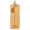 A 35" x 12" Maple rubber wood cutting board with thick handle, gold spreader, and ribbon, topped with crackers, heart-shaped cheese slices, cured meat, dried orange slices.