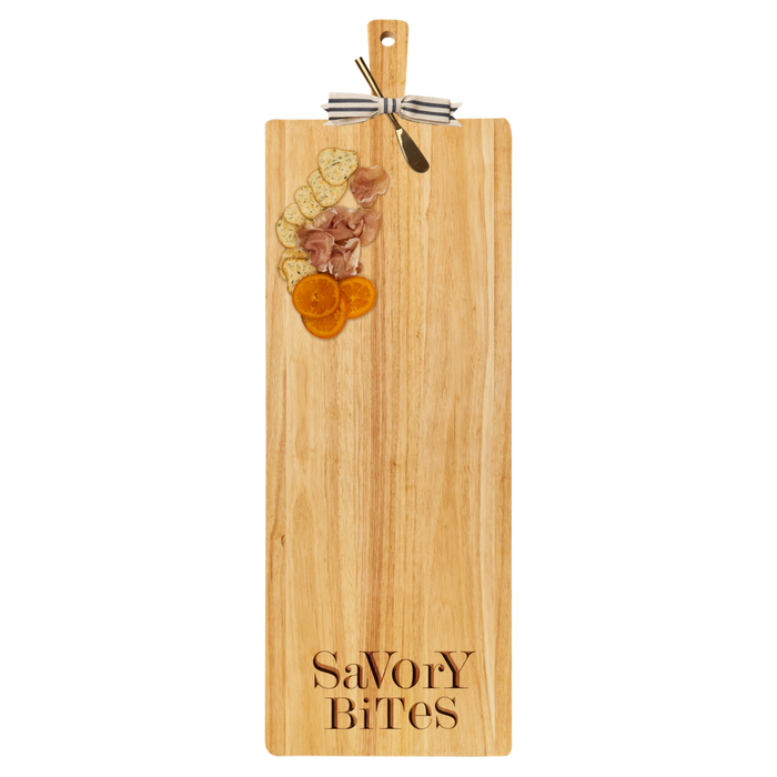 A 35" x 12" Maple rubber wood cutting board with thick handle, gold spreader, and ribbon, topped with crackers, heart-shaped cheese slices, cured meat, dried orange slices.
