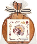 A set of decorative turkey napkins rests elegantly on the Sophistiplate 9.75″ x 8″ Board Gift Kit: Amber Harvest, an acacia wood charcuterie board, wrapped in clear plastic with a striped ribbon and a wooden tag marked M.