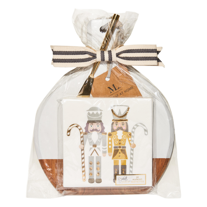 The Maple 9.75" x 8" Board Gift Kit: Gilded Nutcracker includes a round acacia wood board and napkin set with two gold- and silver-accented nutcracker figures, all wrapped in clear plastic with a cream and black striped ribbon.