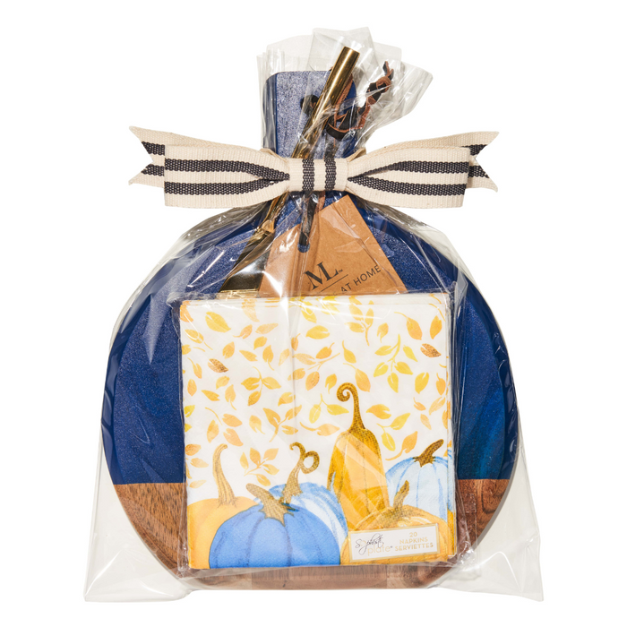 The Maple 9.75" x 8" Board Gift Kit: Harvest Blues includes an acacia wood charcuterie board, a blue pumpkin piece, autumn-themed napkins, and gold utensils—beautifully wrapped with a striped ribbon for a festive touch.