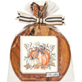The Sophistiplate 9.75" x 8" Board Gift Kit: Turkey and Gourds features a round acacia wood board wrapped in clear plastic with a striped ribbon and a fall-themed napkin showing turkeys and gourds for an autumn touch.