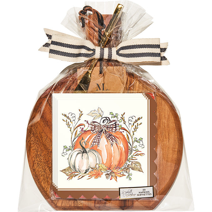 The Sophistiplate 9.75" x 8" Board Gift Kit: Turkey and Gourds features a round acacia wood board wrapped in clear plastic with a striped ribbon and a fall-themed napkin showing turkeys and gourds for an autumn touch.