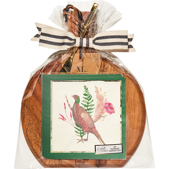 A 9.75″ x 8″ acacia wood board with handle, gold spreader from the Feather Grove collection by Sophistiplate, along with utensils and cocktail napkins featuring a pheasant design, are wrapped in clear plastic and tied with a striped ribbon bow.