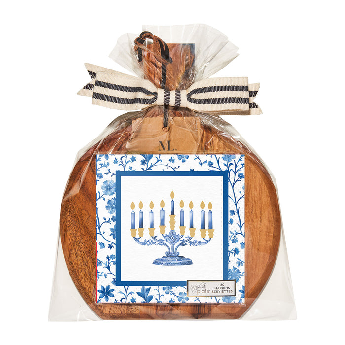 The Sophistiplate 9.75" x 8" Board Gift Kit—Hanukkah Toile features an acacia wood board wrapped in clear plastic with a black-and-white bow and a decorative Hanukkah cocktail napkin displaying a blue menorah and floral border.