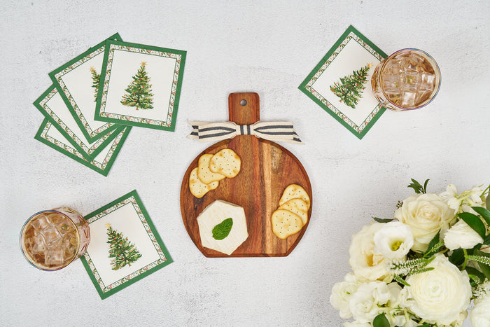 A Sophistiplate Home for the Holidays 9.75" x 8" Board Gift Kit holds crackers and cheese on a white surface, accented by Christmas tree napkins, two iced drinks, and a bouquet of white flowers.