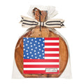 The Sophistiplate 9.75" x 8" Board Gift Kit, "Party in the USA," features a round acacia wood board wrapped in clear plastic with a decorative bow and an M monogram, plus American flag cocktail napkins—perfect for serving appetizers.