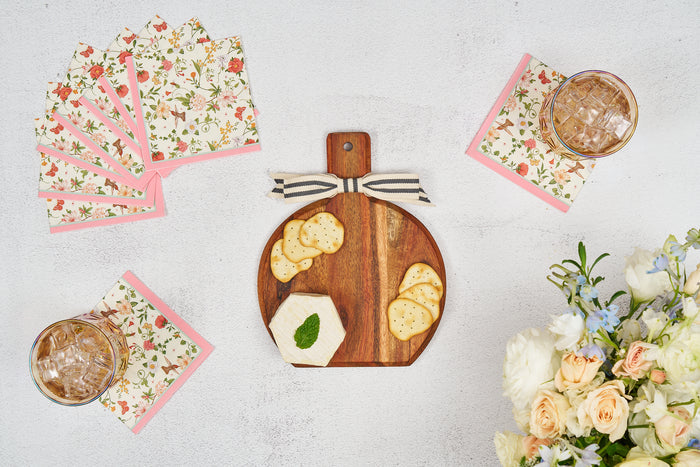 A Sophistiplate 9.75" x 8" Rococo Board Gift Kit (w/o spreader) features crackers and mint, with two iced drinks on cocktail napkins, stacked floral napkins, and a bouquet of white and pale peach flowers on a white surface.