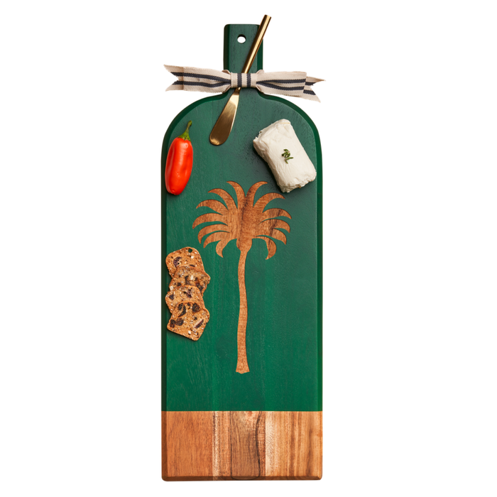 The Maple Acacia Bevel Board Long Green (20 x 7") in Preppy Palm holds a gold spreader, goat cheese, grape tomato, and crisps. The serving board is topped with a striped ribbon.