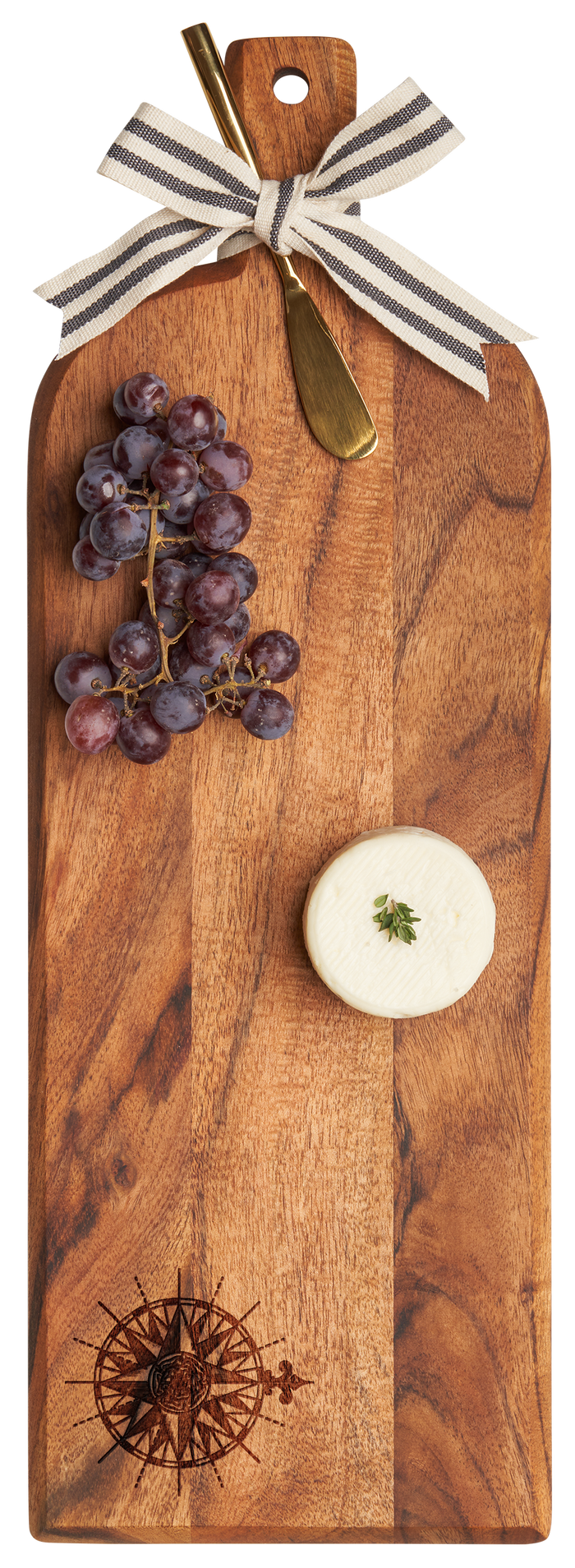 The Maple Acacia Bevel Board w/ Ribbon & Gold Spreader Knife (20 x 7", Compass Rose) displays red grapes and a round cheese topped with thyme, all elegantly arranged with a striped ribbon on the handle.