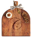 The Maple Acacia Bevel Board with Handle (15 x 12"), personalized and finished food-safe, comes topped with soft cheese garnished with a pecan, two slices of seeded fruit bread, a gold ribbon, and a gray/white spreader.