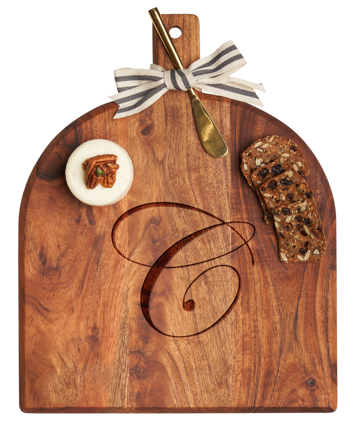 The Maple Acacia Bevel Board with Handle (15 x 12"), personalized and finished food-safe, comes topped with soft cheese garnished with a pecan, two slices of seeded fruit bread, a gold ribbon, and a gray/white spreader.