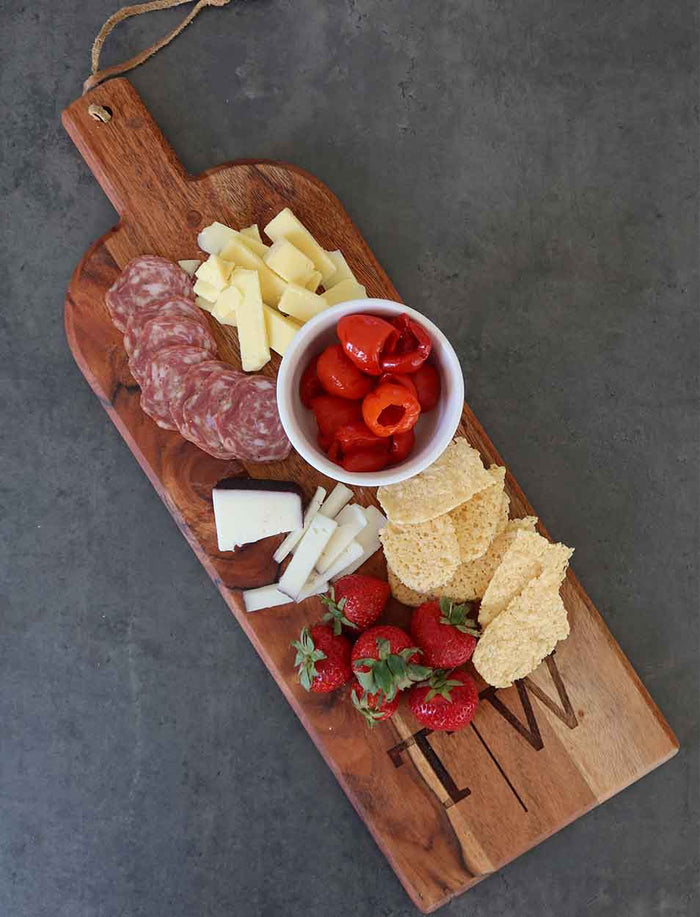 A Maple Acacia Bevel Board with Long Handle (20 x 7") displays salami slices, cheese cubes, stuffed red peppers, tortilla chips, and strawberries—perfectly arranged for a unique personalized gift set.
