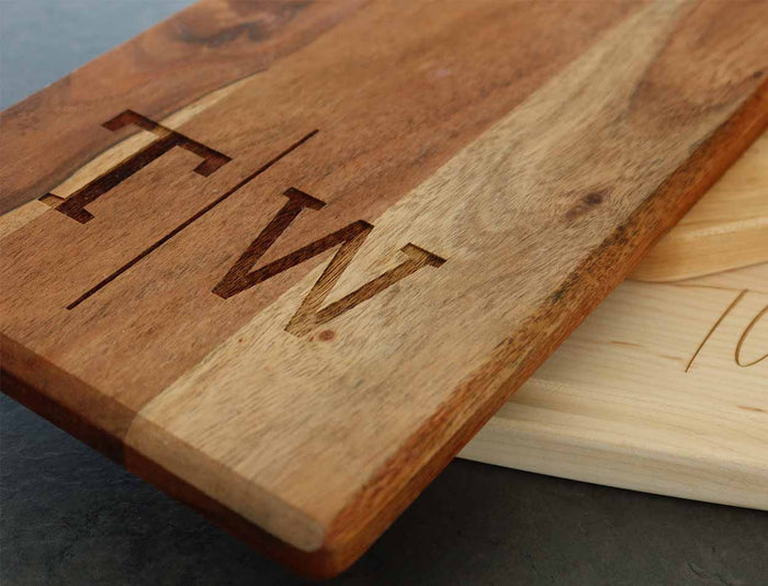 A close-up of Maple's 20x7" Acacia Bevel Board with Long Handle, engraved with a personalized monogram (T|W)—a stylish wooden piece perfect for an elegant gift set.