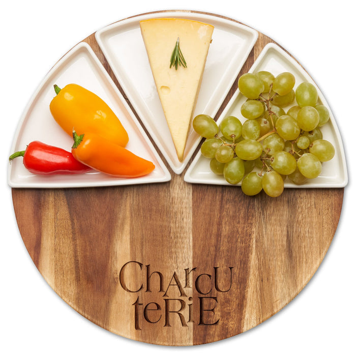 The Maple Acacia Fête Set Round | Charcuterie | 12" Round features a round Acacia wood board engraved with “Charcuterie,” holding three ceramic snack dishes filled with cheese, rosemary, mini peppers, and green grapes.