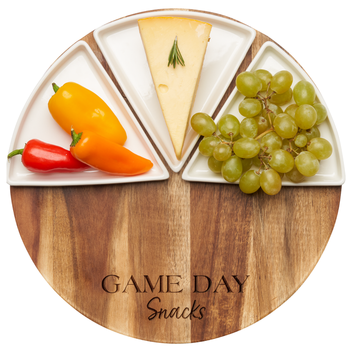 The Maple Acacia Fête Set Round | Game Day Snacks | 12" Round features a round acacia wood board labeled GAME DAY Snacks and three ceramic dishes for serving mini bell peppers, cheese with rosemary, and green grapes.