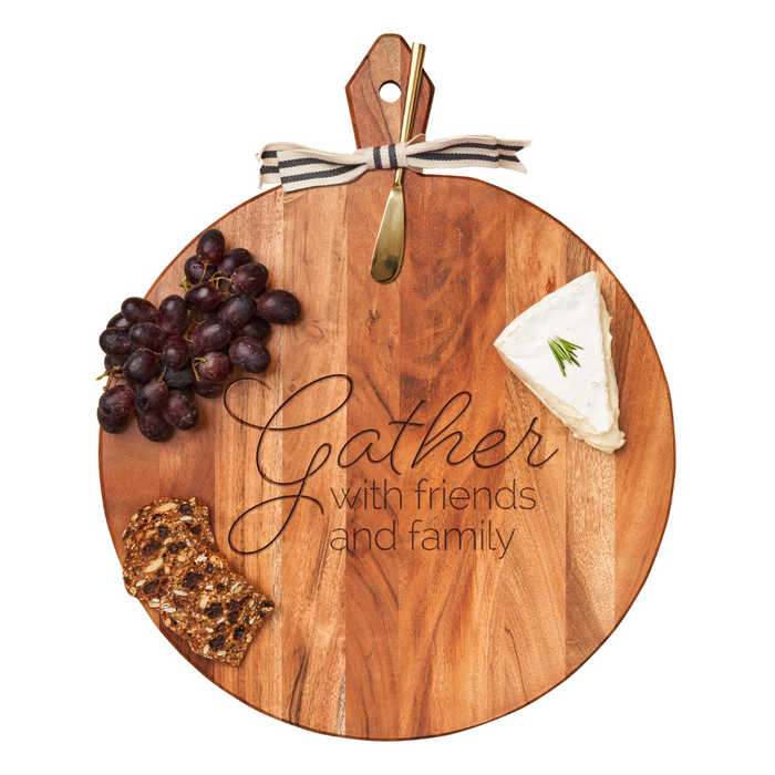 The Maple Acacia Heirloom Board (20x16") is a round charcuterie board engraved with "Gather with Friends and Family," featuring a gold spreader and striped ribbon on the handle.