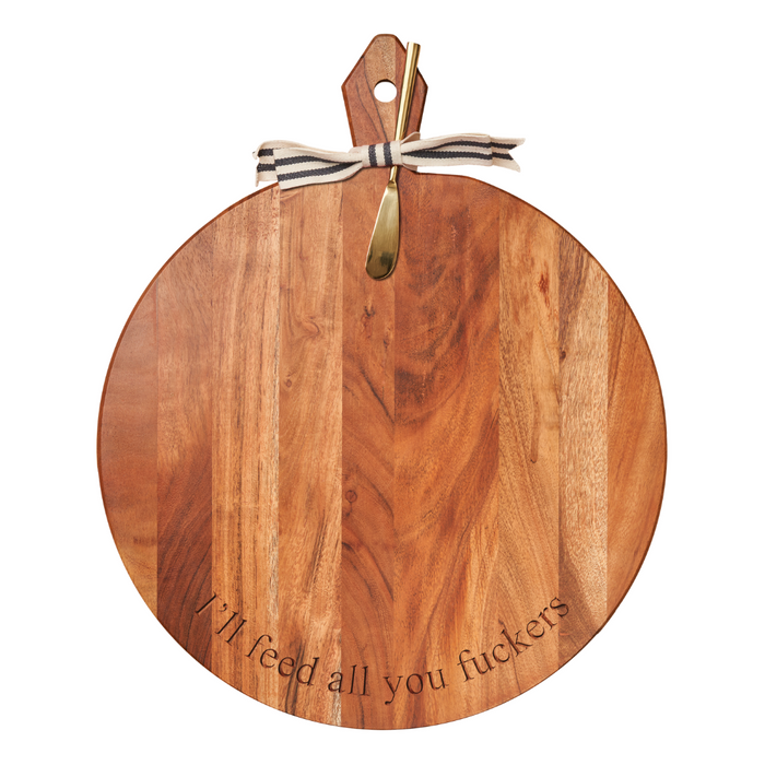 The Maple Acacia Heirloom Board, 20 x 16", is a round charcuterie board with a gold spreader and striped ribbon, engraved with “I’ll Feed All You Fuckers”—a bold statement piece for stylish entertaining.