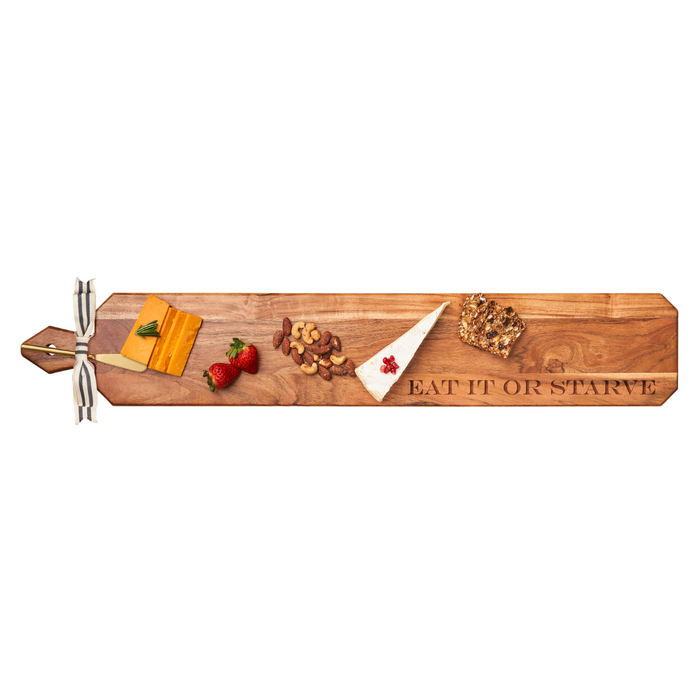 A charcuterie board with cheese, strawberries, nuts, brie, and bread is served on the Maple Acacia Heirloom Board Skinny (34 x 6") engraved with “Eat It Or Starve” and includes a gold spreader and ribbon.