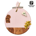 The Maple Acacia Heirloom Board with Handle, Round in Blush (20 x 16"), is shown with a metal cheese knife, crackers, blue cheese, grapes, ribbon bow, and engraved monogram DS. Text reads: Personalize This Item!.