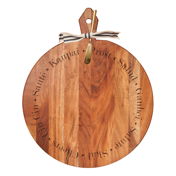The Maple Acacia Heirloom Board features a round acacia wood design with "cheers" engraved in various languages, a leather loop, gold spreader, and striped ribbon—ideal for serving or personalizing with a monogram. Size: 20 x 16".
