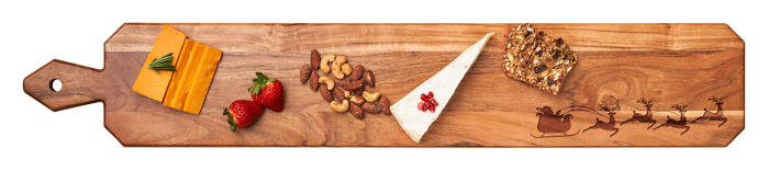 The Maple Acacia Heirloom Board w/ Handle Skinny (34" x 6") features Santa's sleigh with reindeer, perfect for elegantly serving cheddar slices, brie with pomegranate, strawberries, and more to delight any charcuterie lover.