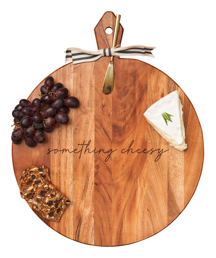The Maple Acacia Heirloom Board with Handle (20 x 16 x .6") features "something cheesy" engraving, comes with a gold spreader tied with a gray & white ribbon, and is styled with cheese wedge, red grapes, and seeded crispbread.