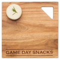 A round cheese with rosemary rests on Maple's Acacia Modern Geo Square 12 x 12" board, engraved "GAME DAY SNACKS," which features a triangular cutout in the top right corner.