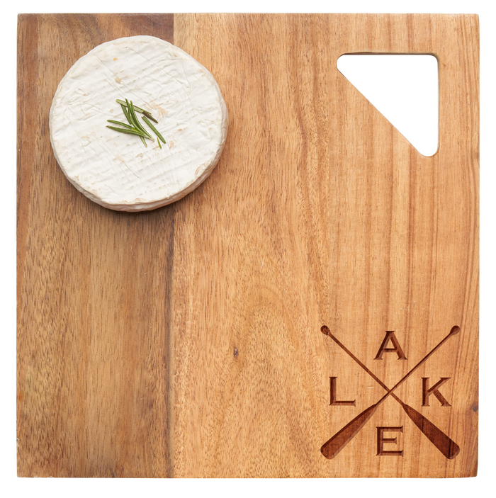 A round wheel of brie with chives sits on the Maple Acacia Modern Geo Square | Lake | 9 x 9" board, which features a triangle cutout and crossed paddle engraving with L, A, K, and E in the lower right corner.