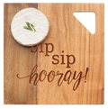 A wheel of cheese with herbs rests on Maple’s Acacia Modern Geo Square Sip Sip Hooray 9 x 9" board—engraved in mixed fonts—perfect for charcuterie.