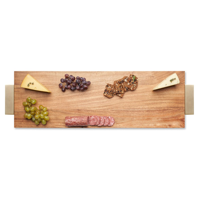 A Maple Acacia Serving Board with Gold Handles (30 x 10") displays two cheese wedges, green and purple grapes, sliced salami, and crackers, all neatly arranged against a white background.