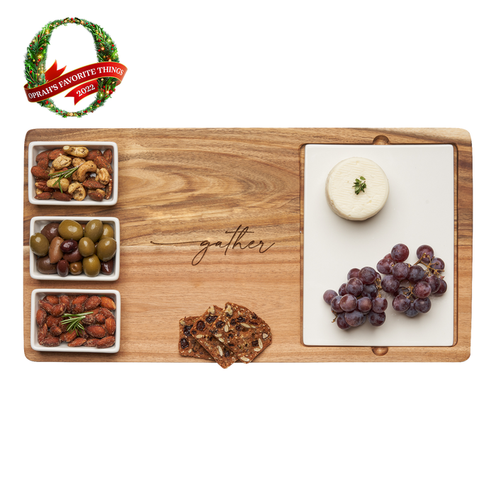 The Maple Acacia Wood Fête Set with "gather" engraving, an Oprah's Favorite, features three ceramic snack dishes for nuts, olives, and almonds. Crackers, grapes, and cheese surround it in a festive display.