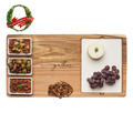The Maple Acacia Wood Fête Set with "gather" engraving, an Oprah's Favorite, features three ceramic snack dishes for nuts, olives, and almonds. Crackers, grapes, and cheese surround it in a festive display.