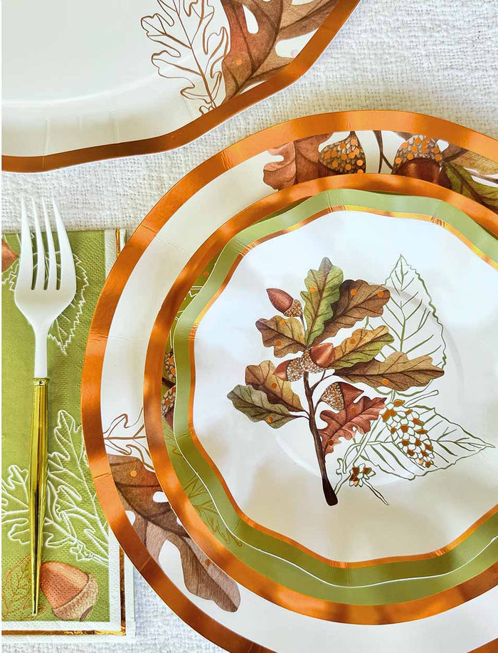 Sophistiplate’s Acorn and Oak Collection paper plates and napkins, adorned with autumn leaf and acorn motifs, are arranged on a textured white surface. A white plastic fork and a gold-handled knife rest atop a green napkin with embroidered leaves, beautifully accenting the fall-themed Thanksgiving plates. For serving sides or desserts, complete your tablescape with the matching Sophistiplate Acorn and Oak Appetizer/Dessert Bowls (8pk) for effortless entertaining.